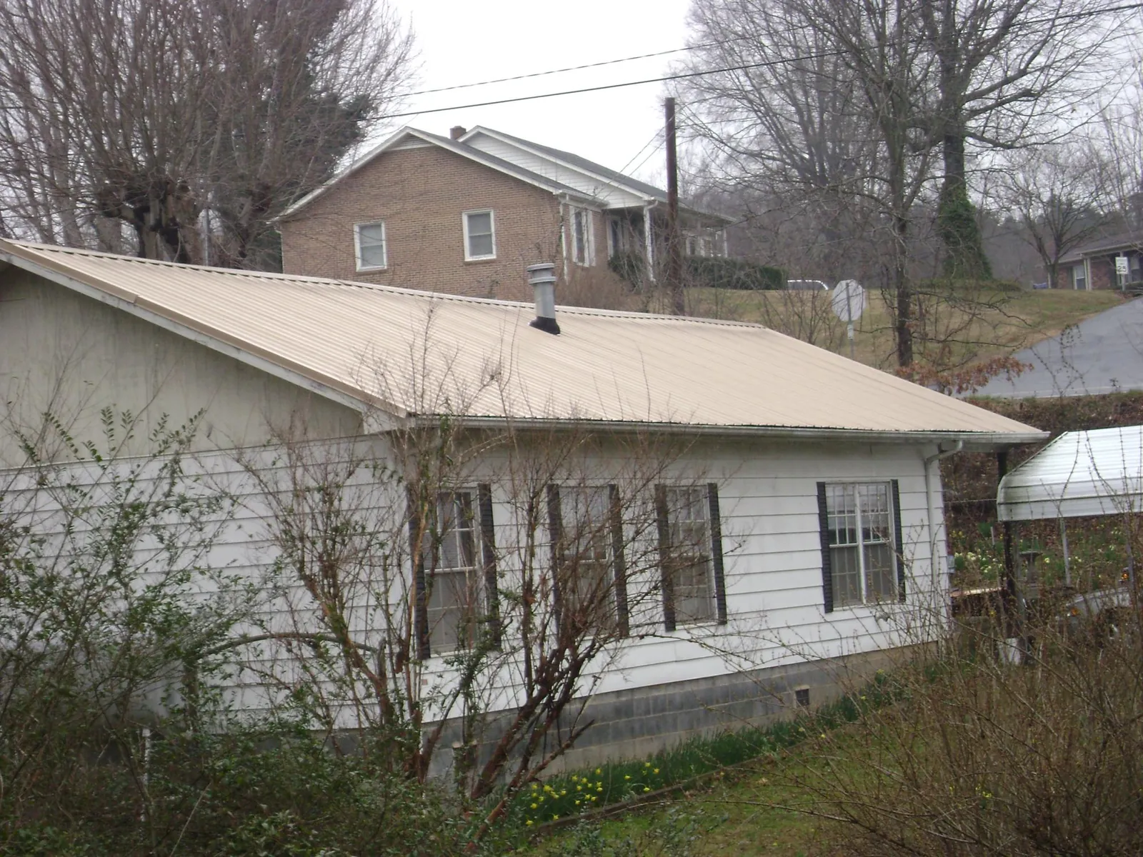 Tan metal roof on a white sided house set into a hillside — Commercial Roofing by Roofing Brothers in Sierra Vista